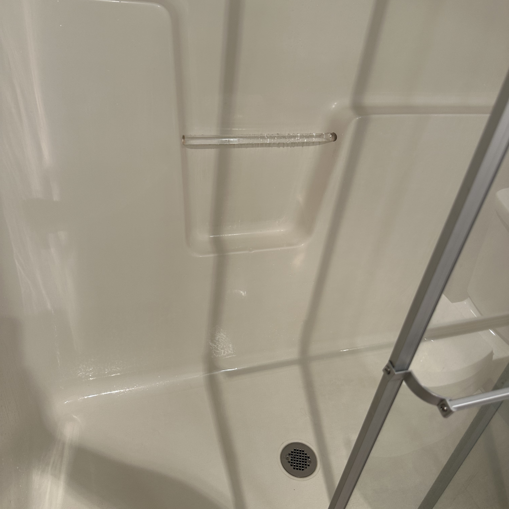 Interior of a clean, white shower stall with a glass door, featuring a built-in shelf and a drain at the bottom